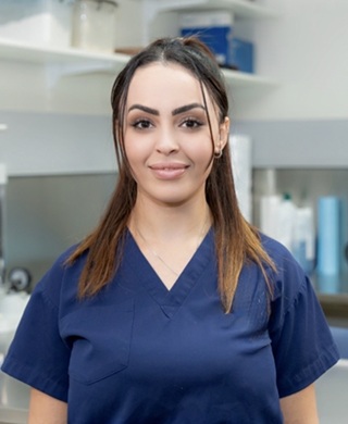 Female healthcare professional in navy scrubs smiling in a clinical setting.